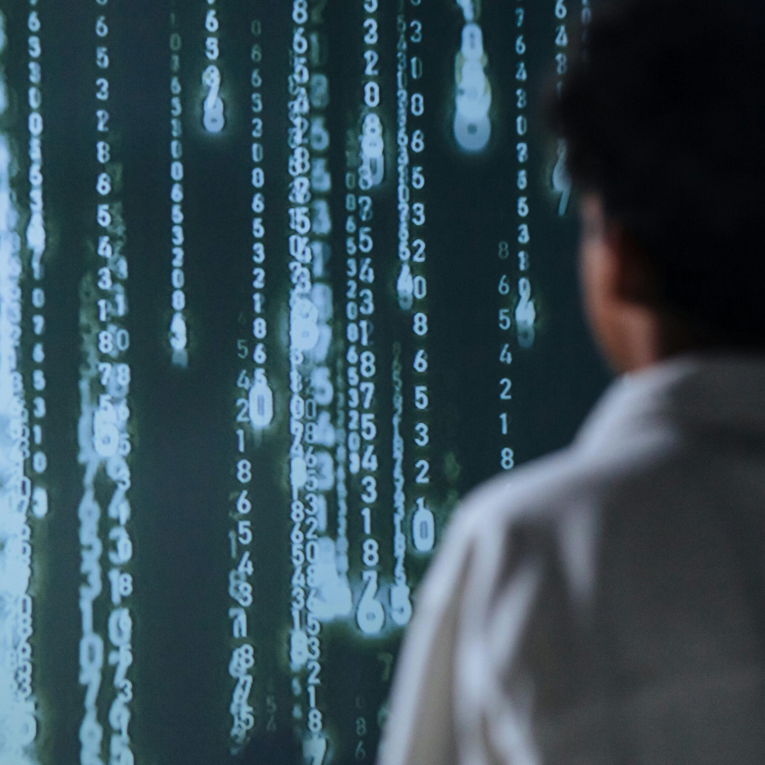 Eine Person blickt auf eine Matrix-artige Wand mit Informationen.